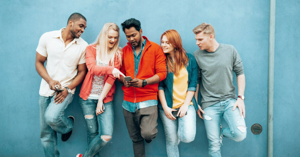 A diverse group of Generation Z standing against a wall using digital technology